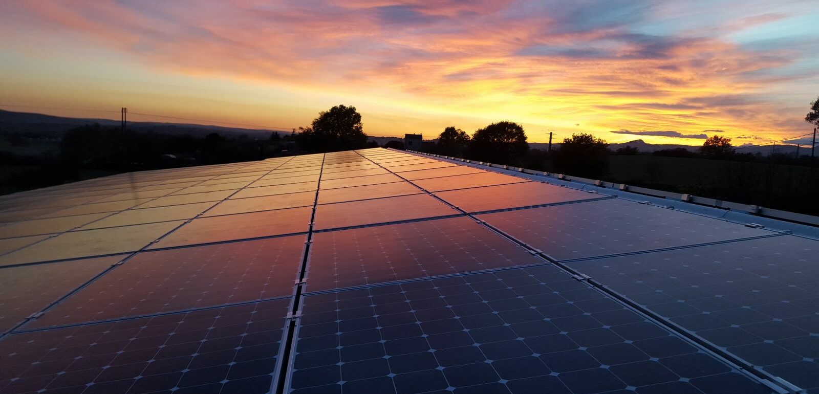 panneaux photovoltaiques sur un toit avec le coucher de soleil, en arrière plan et un ciel rose - orangé. Symbolise les économies d'énergie réalisées grâce aux panneaux solaires dans l'Hérault.