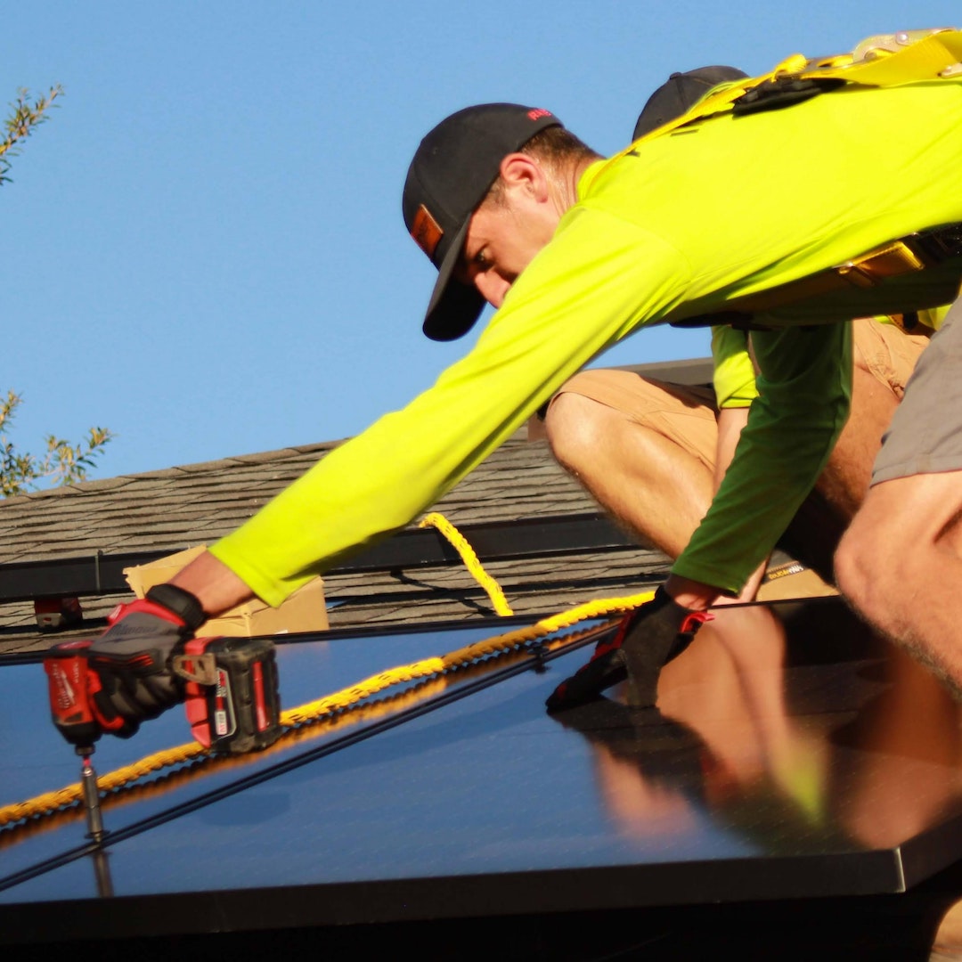 Installateur de panneaux solaires habillé d'un tee-shirt jaune, d'une casquette et de gants de protection intervenant sur un toit pour fixer les panneaux photovoltaïques et réaliser des économies d'énergie dans l'hérault.
